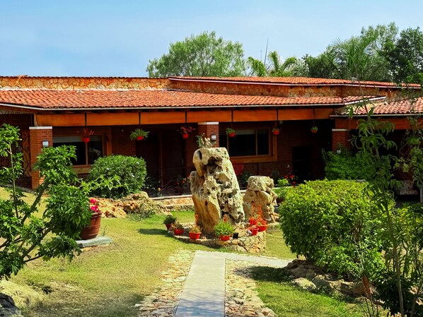 A building with a red-tiled roof, a stone facade, and a garden with potted plants and a rock feature. - Hotel Boutique Matea (Ixtapan de la Sal)