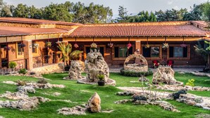 Um edifício rústico com telhado de cerâmica, fachada de pedra e um jardim bem cuidado, com pedras e plantas em vasos.