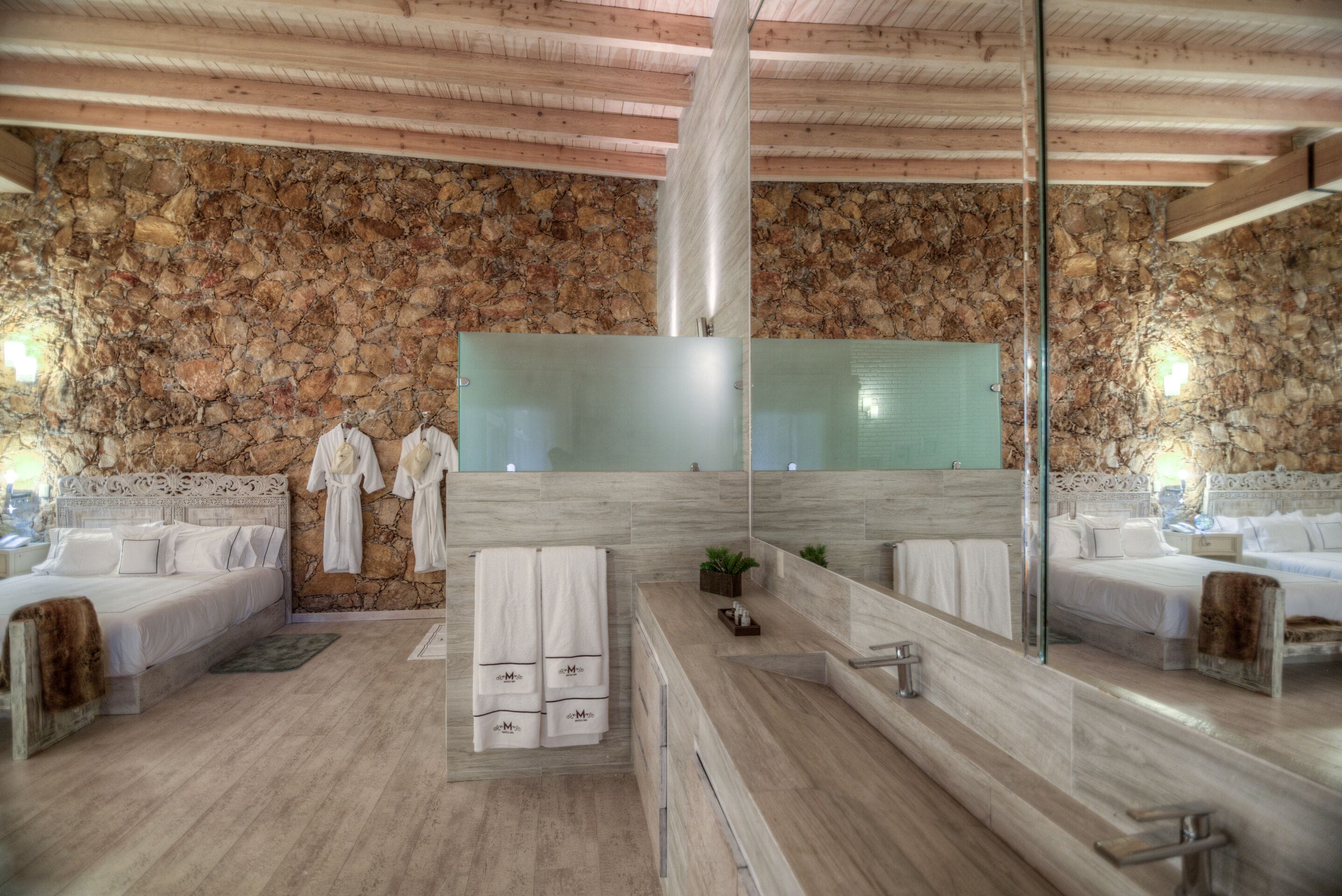 Un baño moderno con pared de piedra, un espejo grande y techo de madera.