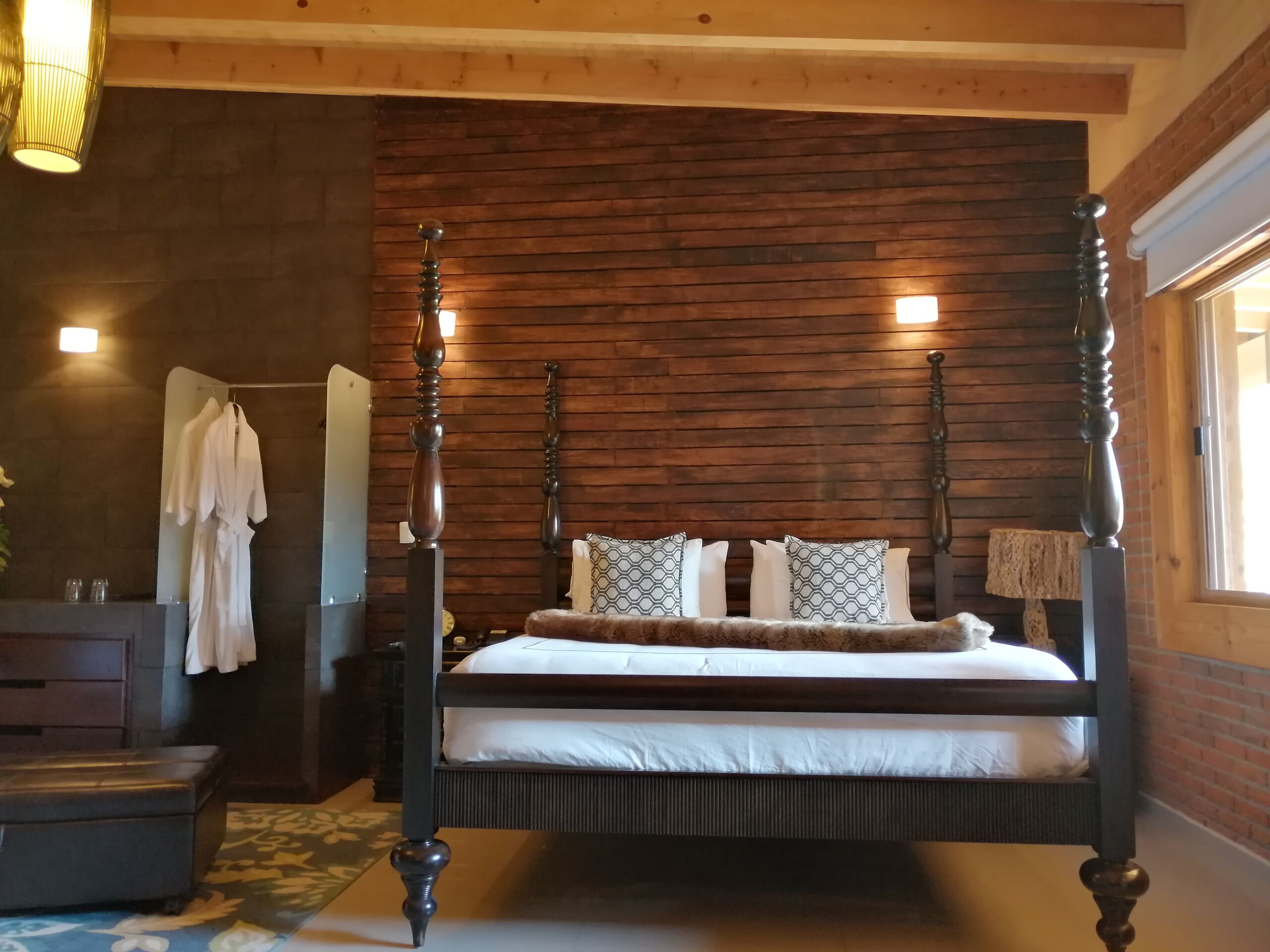 A four-poster bed with a wooden headboard, a mirror, and a bedside table with a lamp.
