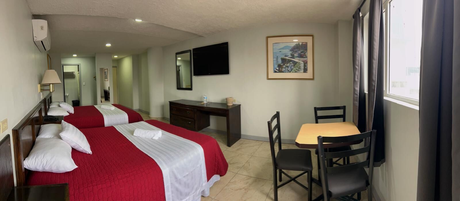Une chambre d’hôtel avec deux lits, un bureau, une chaise, une télévision et une fenêtre avec des rideaux.