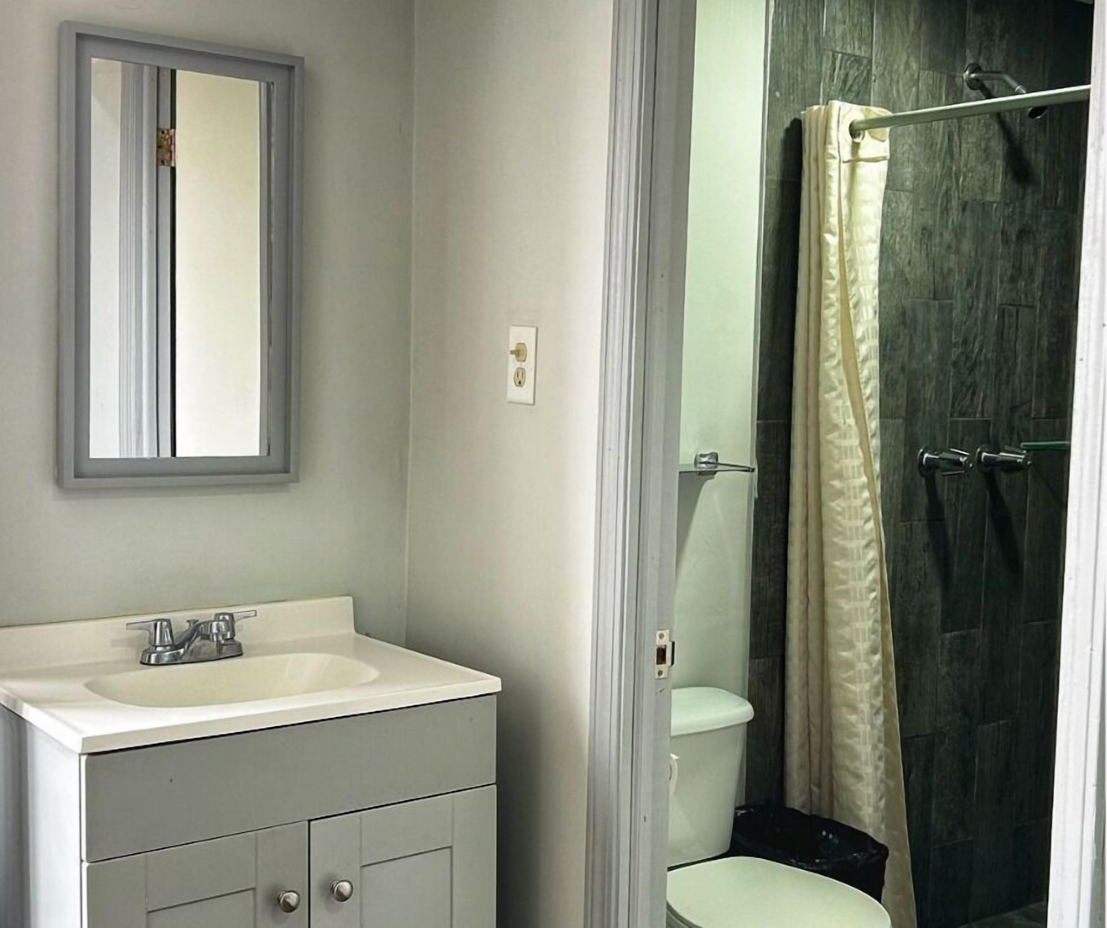 A bathroom with a white sink, a mirror, and a shower with a beige curtain.