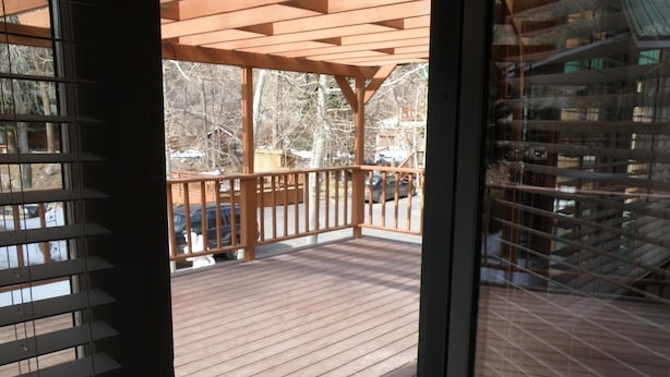 A wooden deck with a railing, a covered area, and a view of trees and a building in the background. - The River's Edge Motel Lodge & Resort (Ouray)