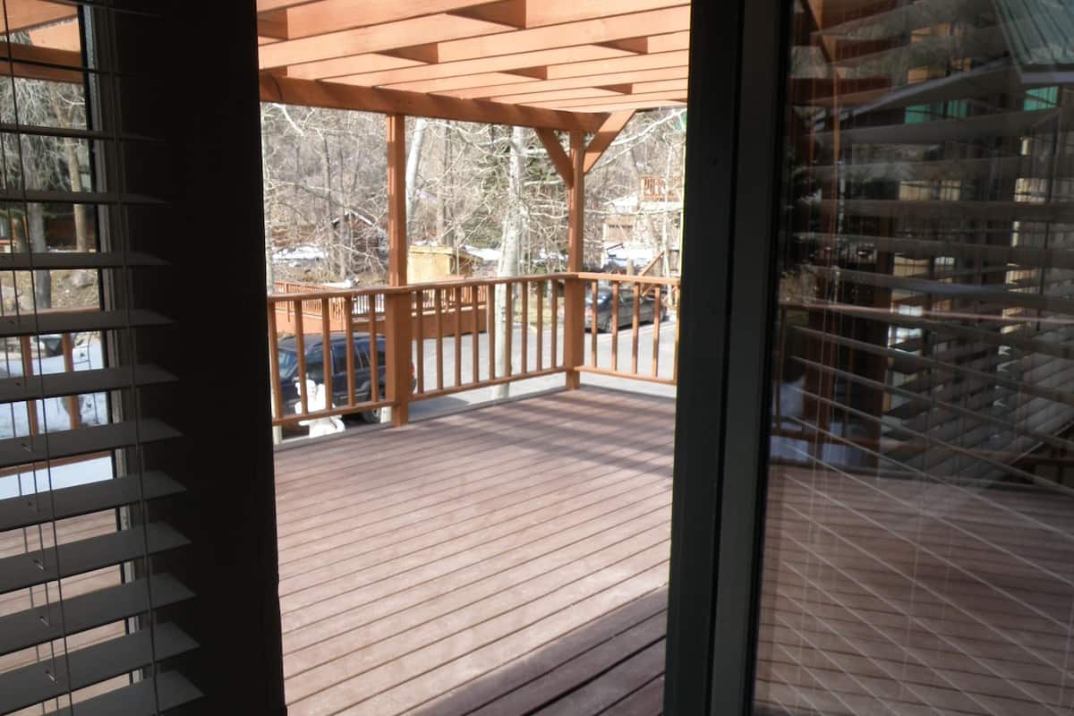 A wooden deck with a railing, a covered area, and a view of trees and a building in the background.