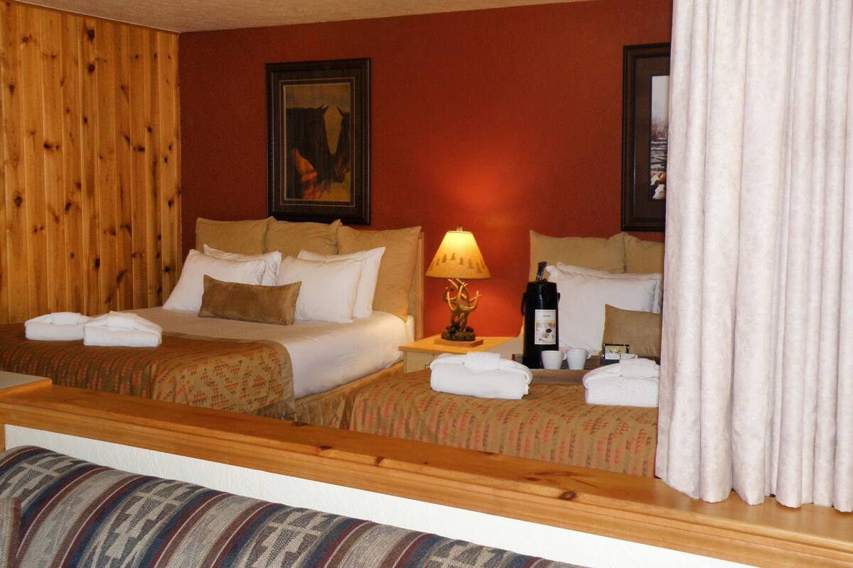 A hotel room with two beds, a wooden headboard, a framed picture, a lamp, a bottle, and a mirror.