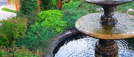 Un giardino con una fontana a più livelli, circondato da vegetazione lussureggiante e piante fiorite.