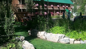 A two-story lodge with a green roof, surrounded by a well-maintained garden with rocks and shrubs. - The River's Edge Motel Lodge & Resort (Ouray)