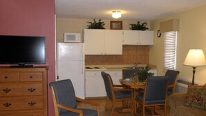 A compact living space with a kitchenette, a dining area with two chairs, a sofa, a television, and a lamp. - The River's Edge Motel Lodge & Resort (Ouray)