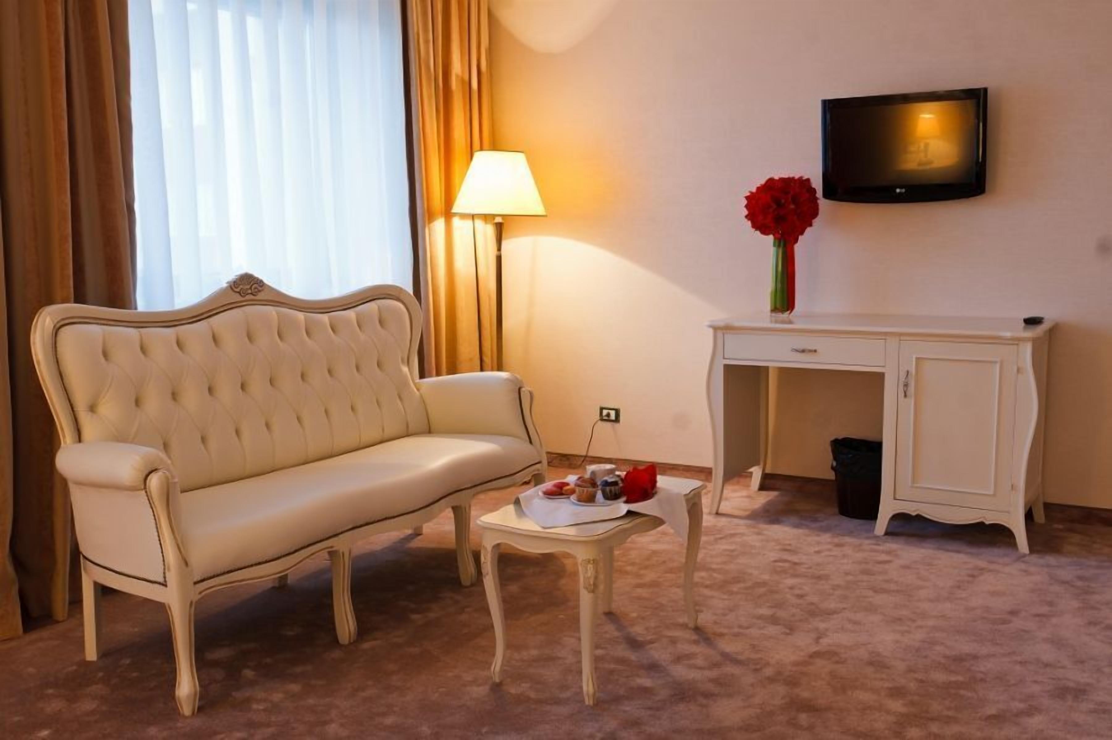 Une chambre d’hôtel avec un canapé beige, une petite table sur laquelle se trouve un plateau de collations, une lampe, un téléviseur et un meuble.