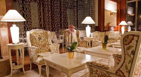A room with floral-patterned furniture, including sofas and armchairs, arranged around a central table. There are two lamps on side tables, and a potted plant on the table. - Hotel Roman By Dumbrava Business Resort (Roman)