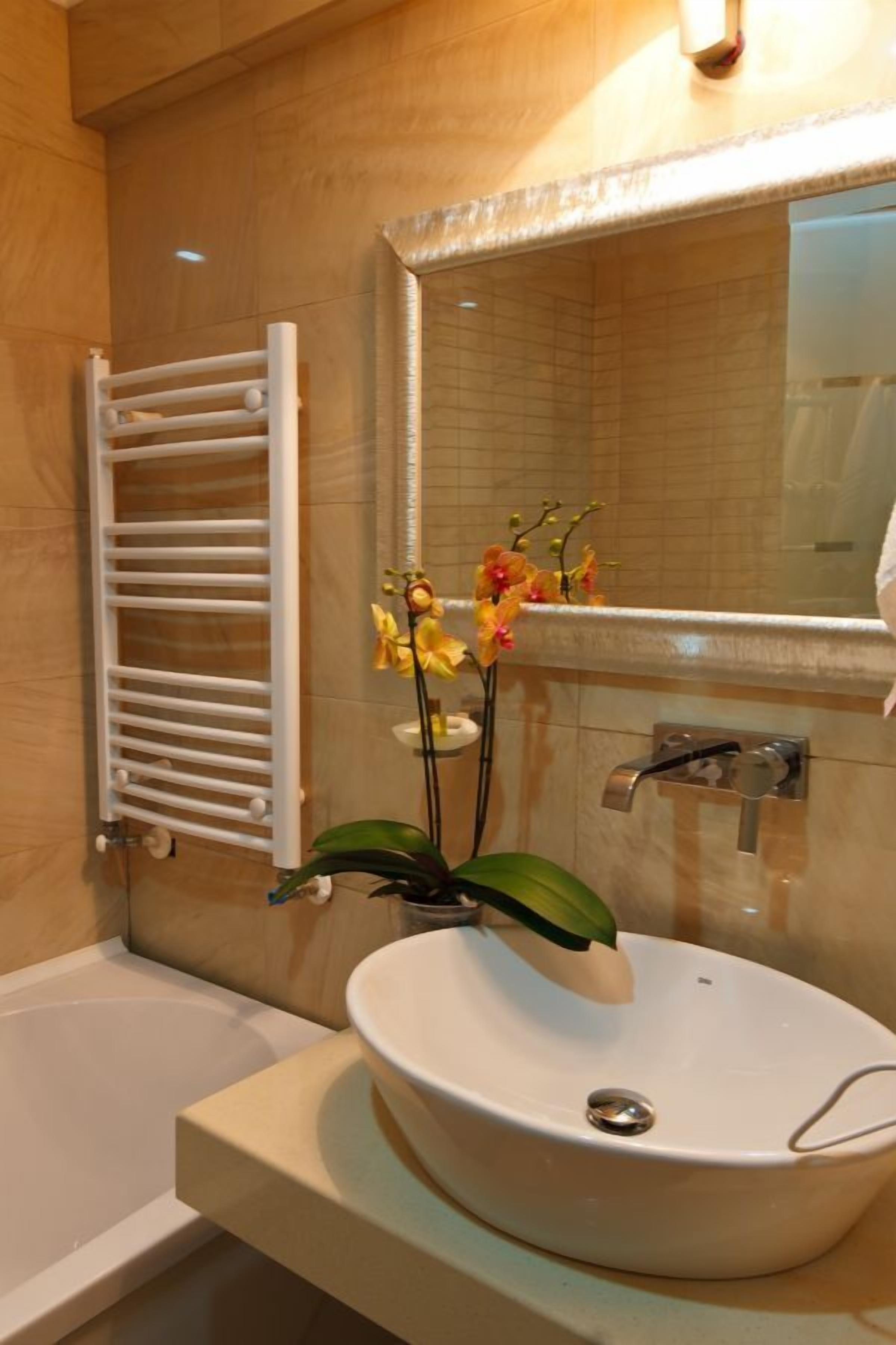 Un baño con bañera, lavamanos, toallero y espejo.