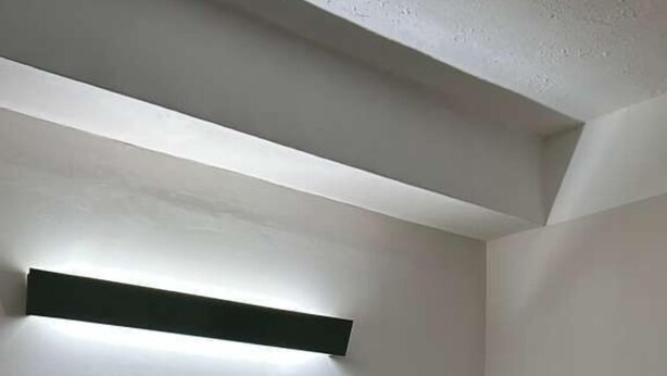 Una cama individual con cabecera, una mesita de noche y una lámpara fijada a la pared.