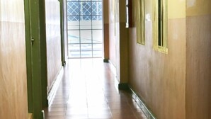 Un pasillo con piso de baldosas, paredes pintadas de verde y una puerta al final que da al exterior.