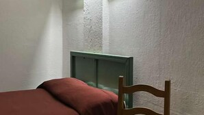 Una habitación pequeña y tenue, con una cama individual, una silla y una mesita.
