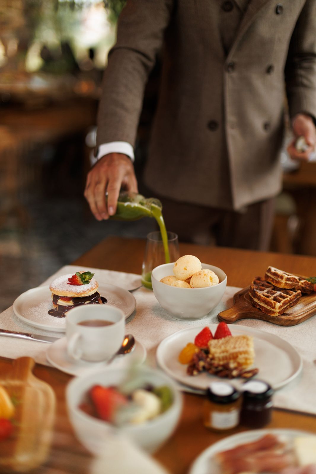 A dining table with various dishes, including a dessert with a strawberry on top, a bowl of round pastries, and a plate of waffles.