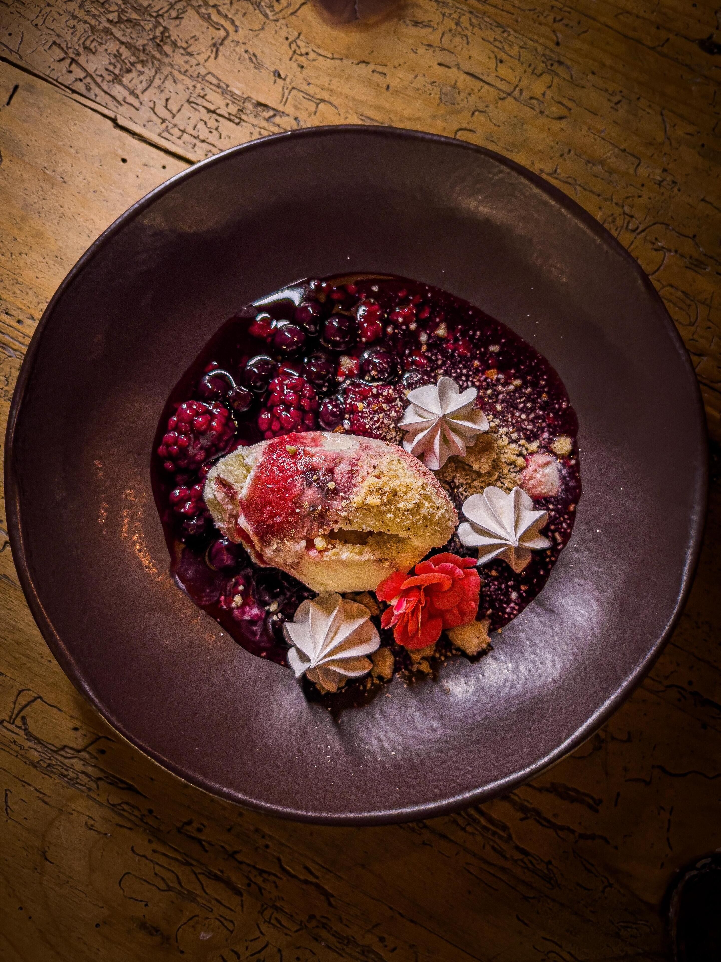 A dessert on a dark plate with berries and decorative elements.