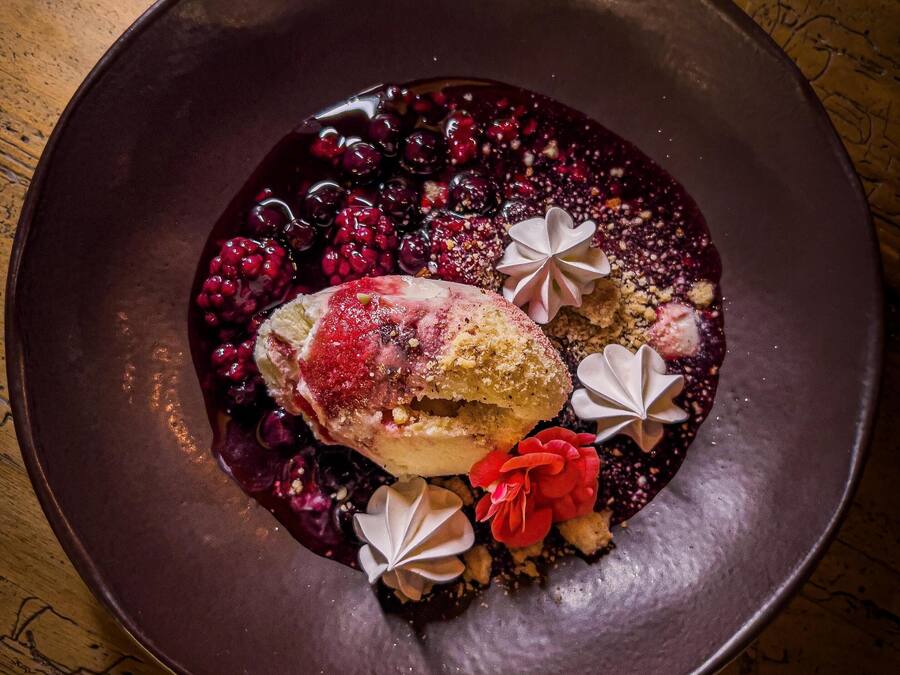 A dessert on a dark plate with berries and decorative elements.
