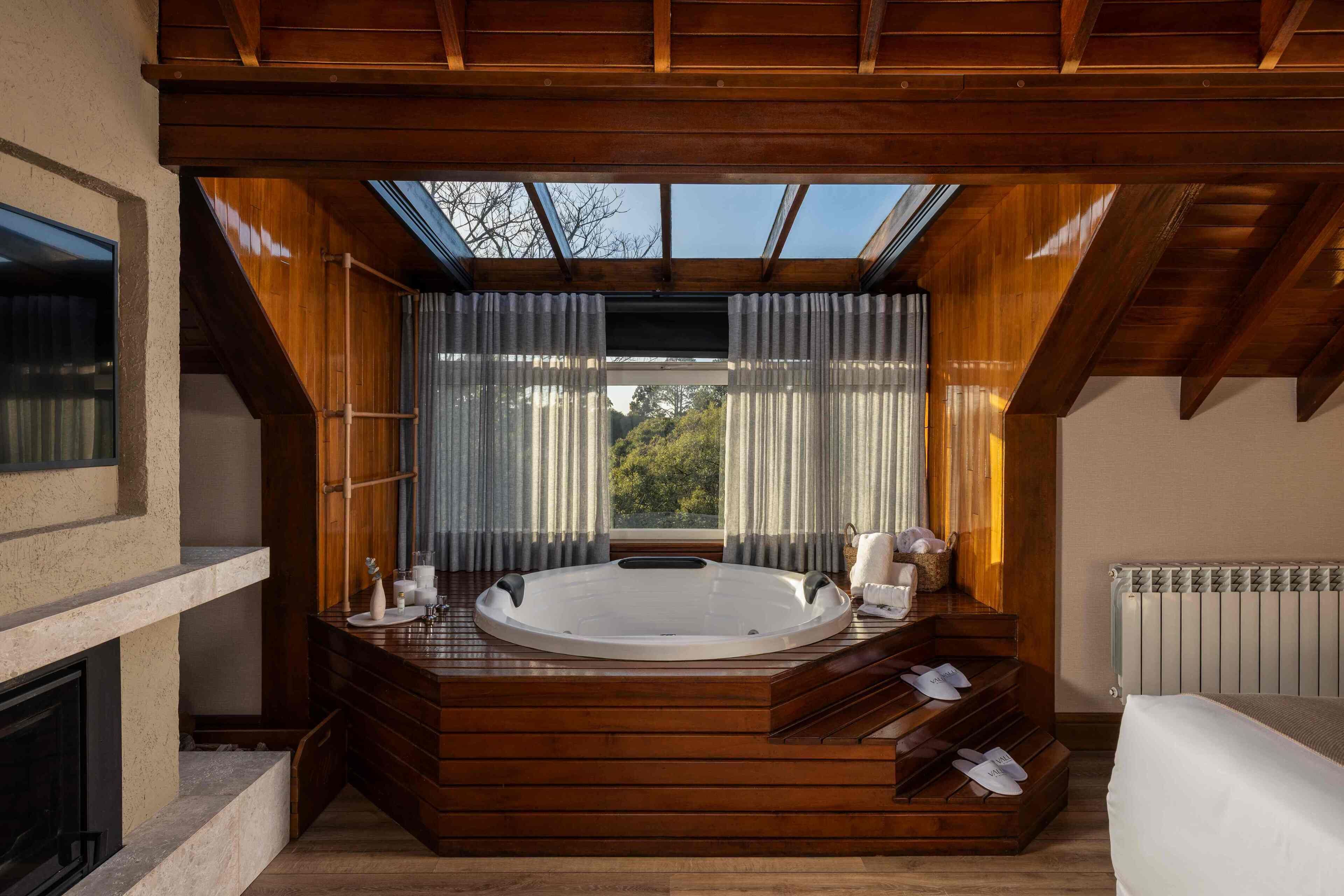 A modern bathroom with a freestanding bathtub, wooden flooring, a skylight, and a view of the outdoors.