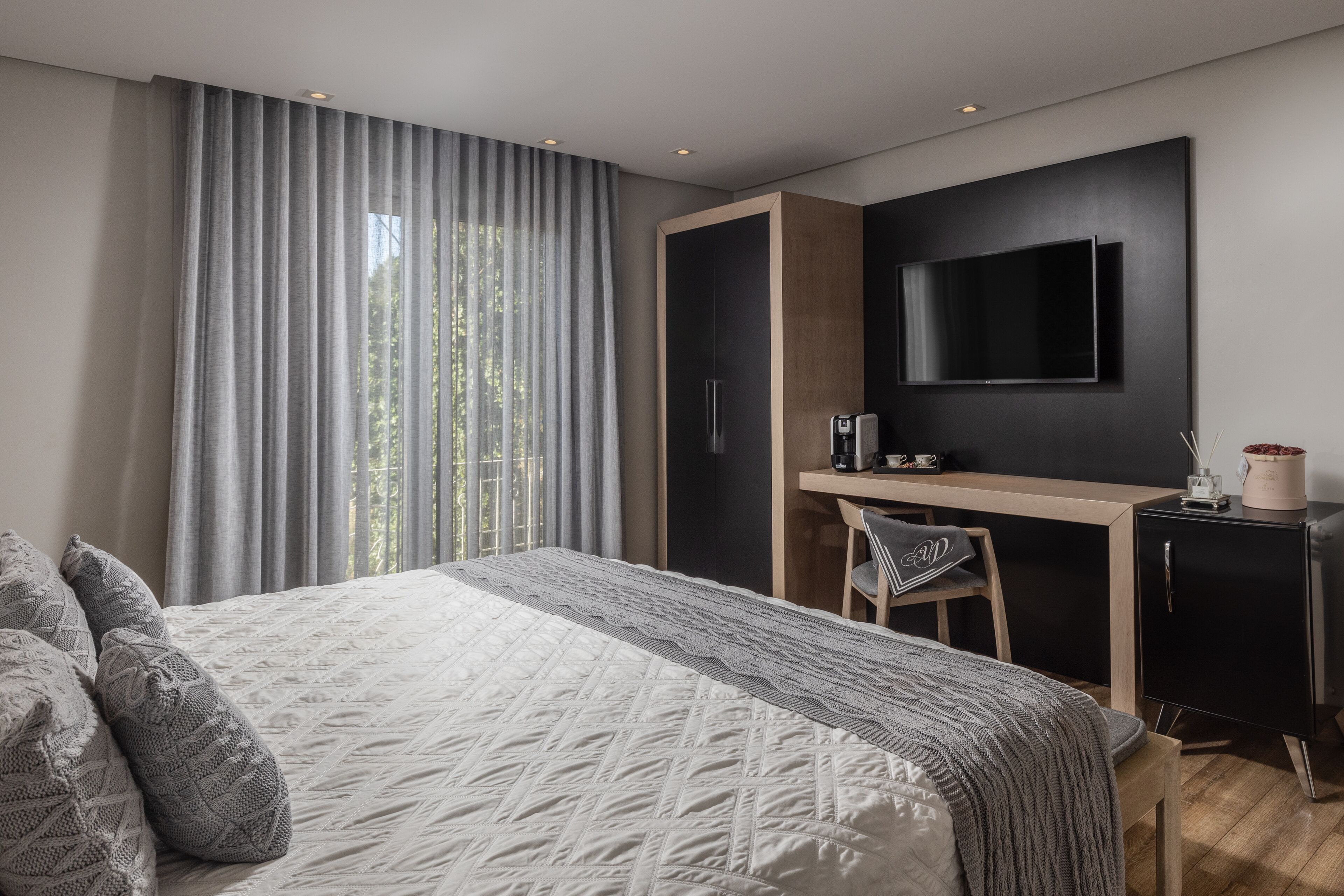 A modern bedroom with a large bed, a desk, a TV, and a wardrobe.