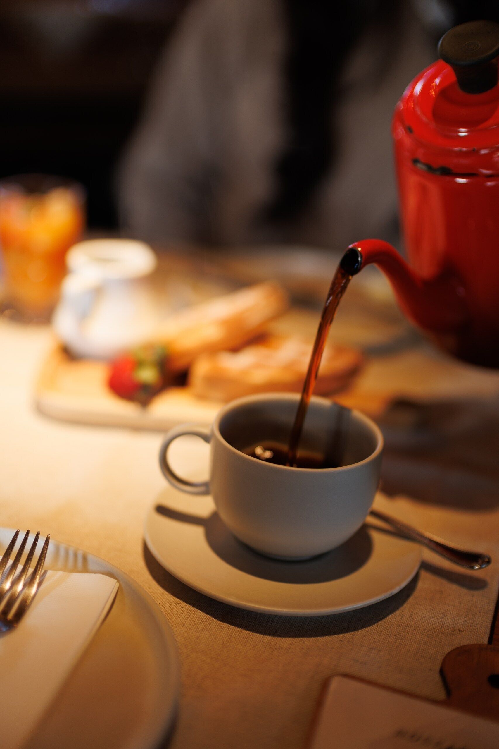 Una taza de café sobre un platito, con una tetera sirviendo en ella.