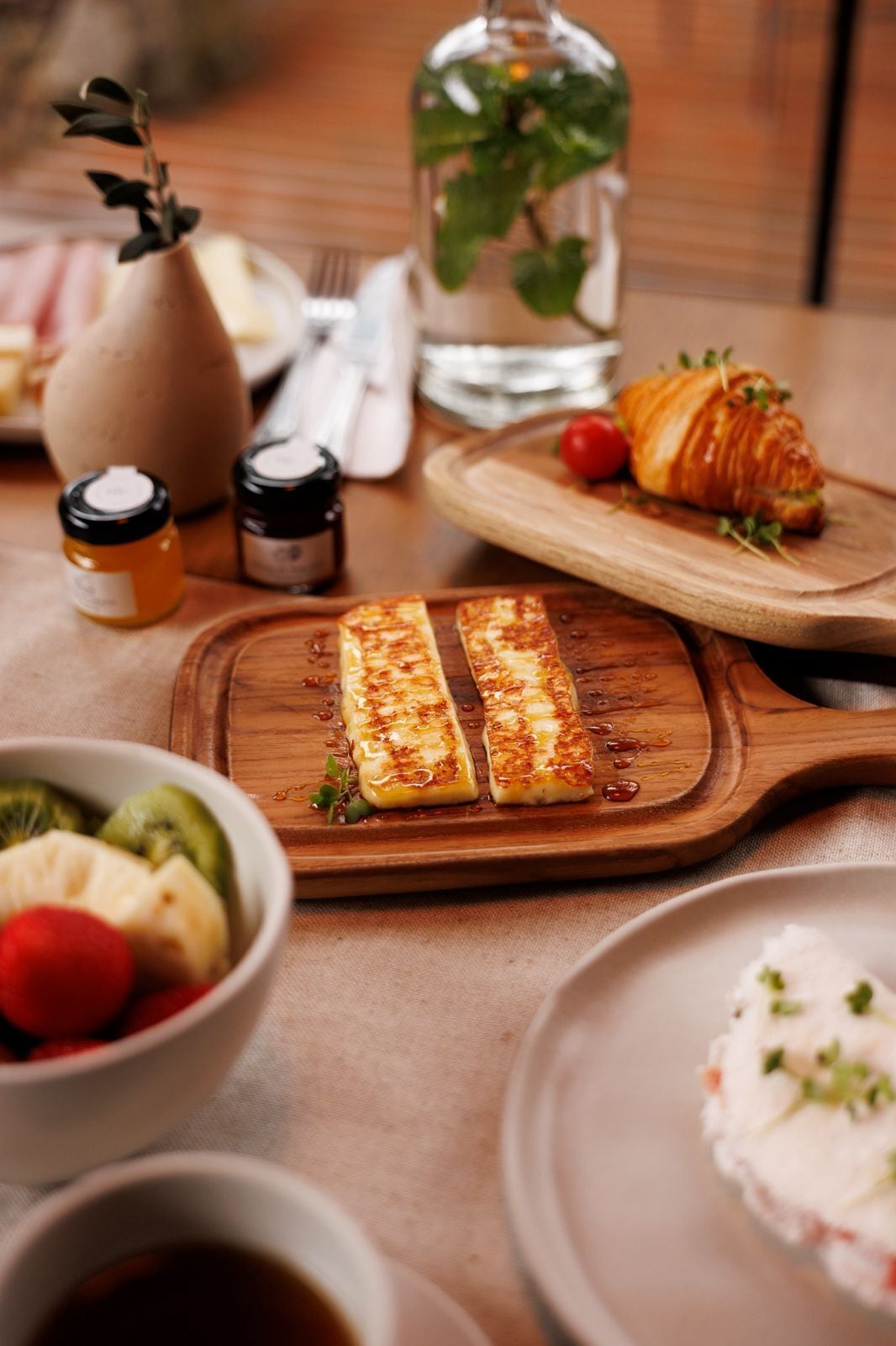 Uma mesa com comidas, incluindo sanduíche de queijo grelhado, croissants e uma tigela de frutas.