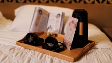 A bed with a wooden tray holding black cups, a wine bottle, and a menu.