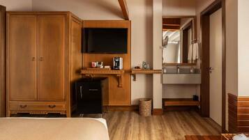A hotel room with a large wardrobe, a flat-screen TV, a minibar, a wooden bench, and a mirror.