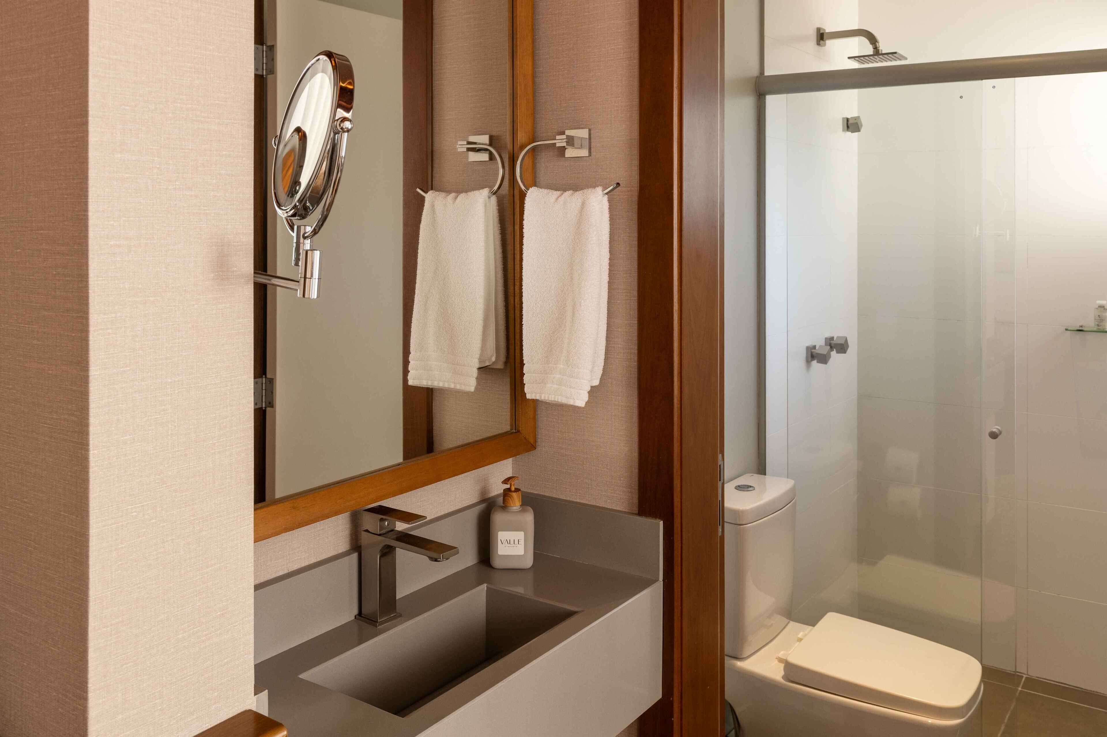 A bathroom with a mirror, sink, towel rack, and a shower enclosure.