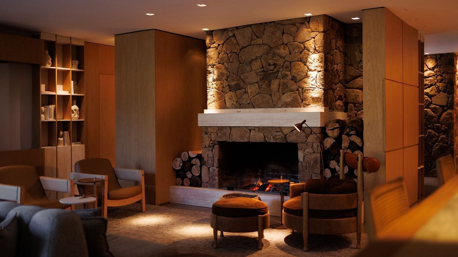 A cozy living room with a stone fireplace, comfortable seating, and a bookshelf.