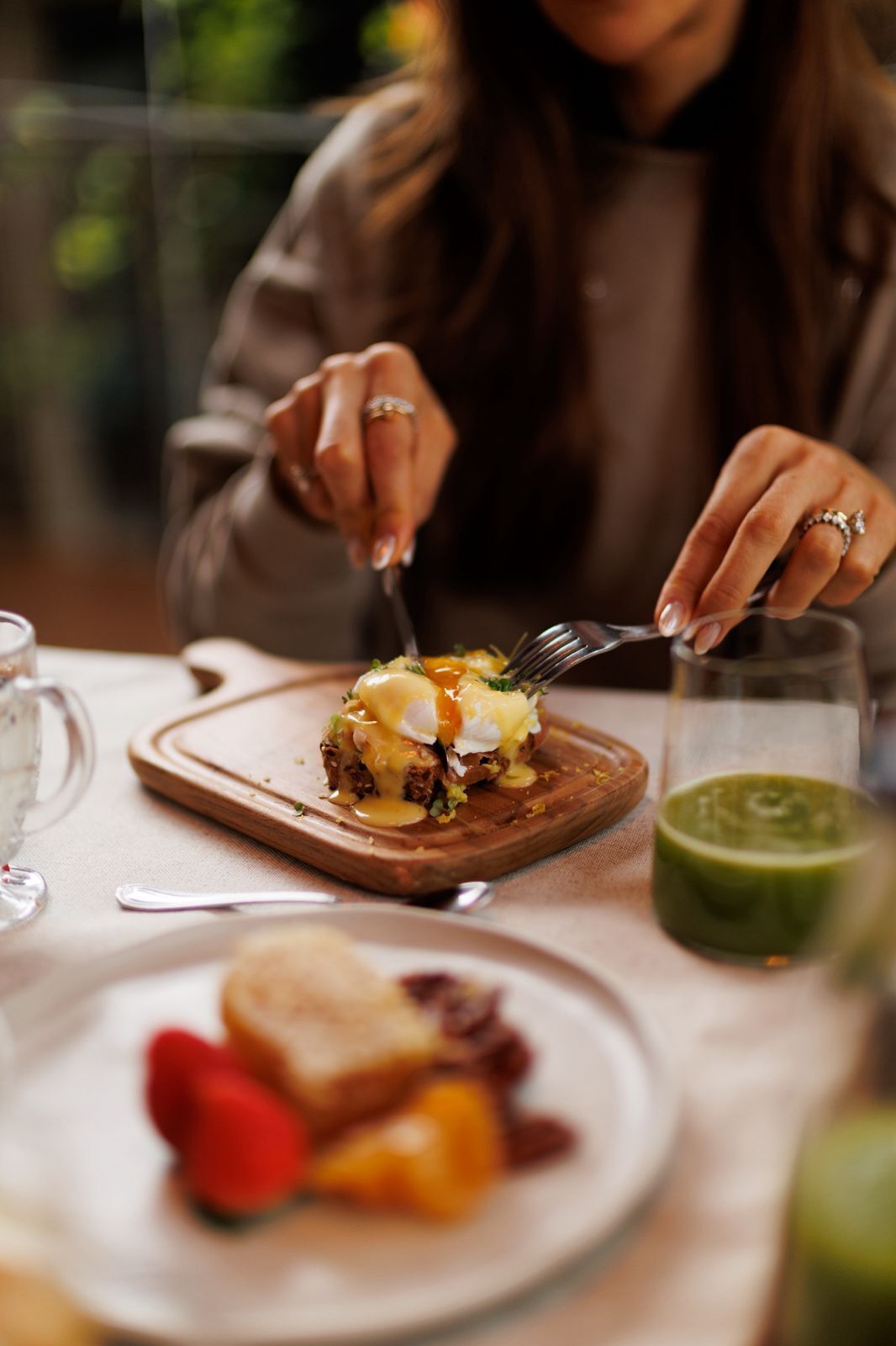 A person dining with a meal on a wooden board, a glass of drink, and a plate with food items.