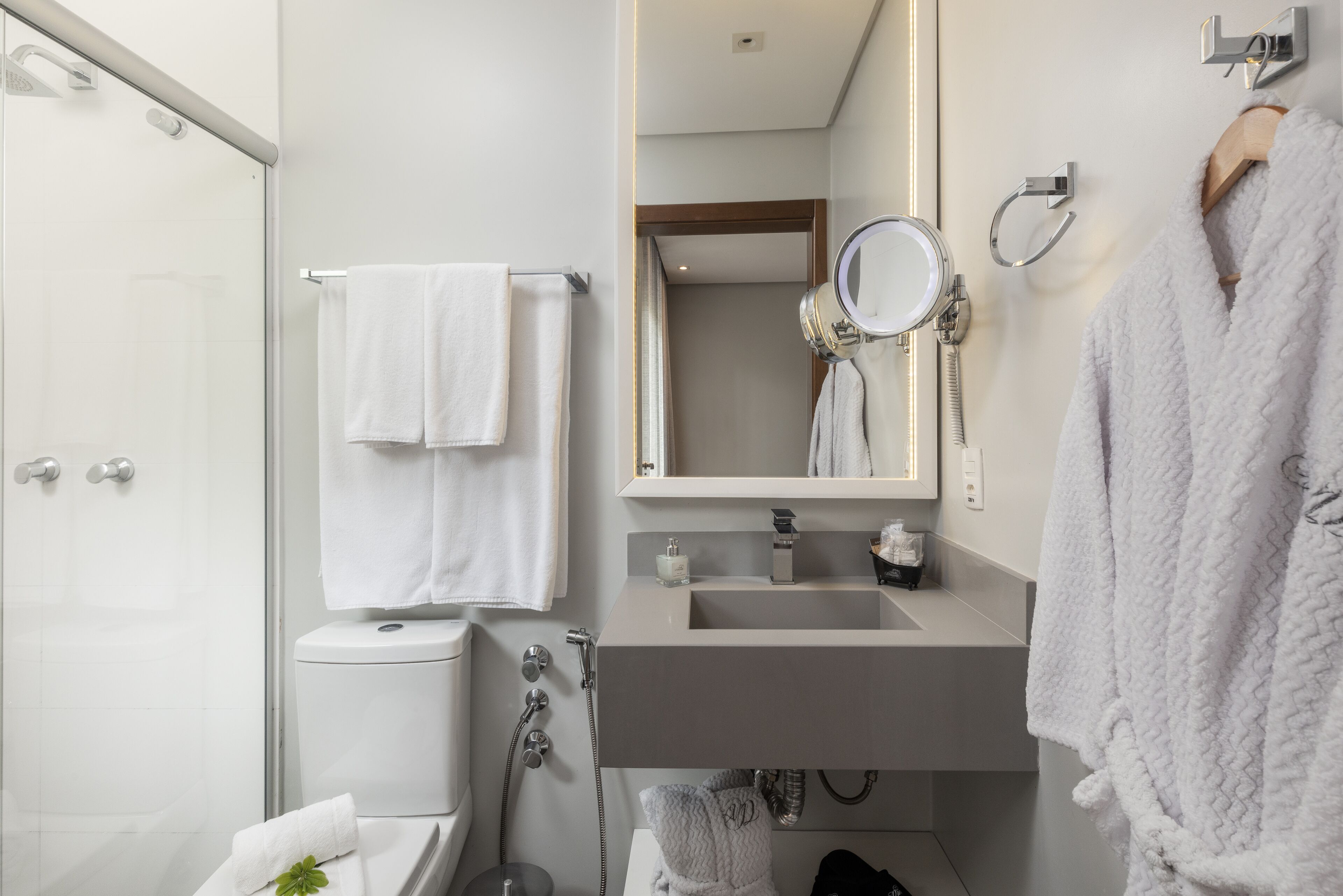 Un baño moderno con cabina de ducha de vidrio, inodoro, lavamanos con espejo y toallero.
