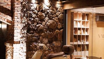 A vintage scooter parked in front of a stone wall with a wooden interior and a glass door leading to a room with shelves.