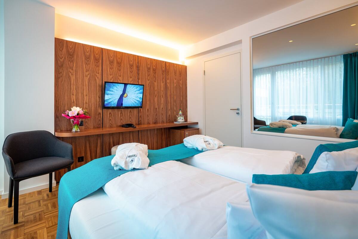 Habitación de hotel con dos camas, un escritorio, una silla, un televisor y un espejo grande.