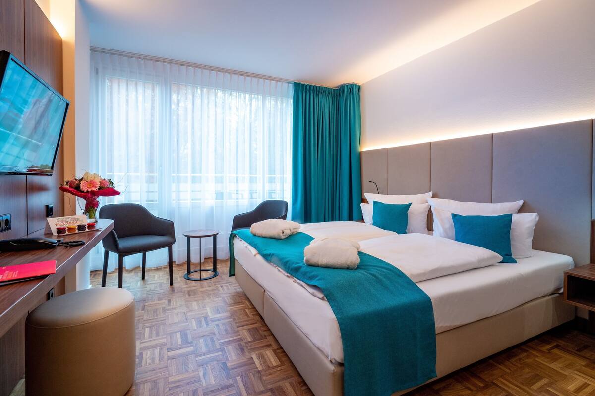 Una habitación de hotel con una cama, un escritorio con computadora, una silla y un televisor.