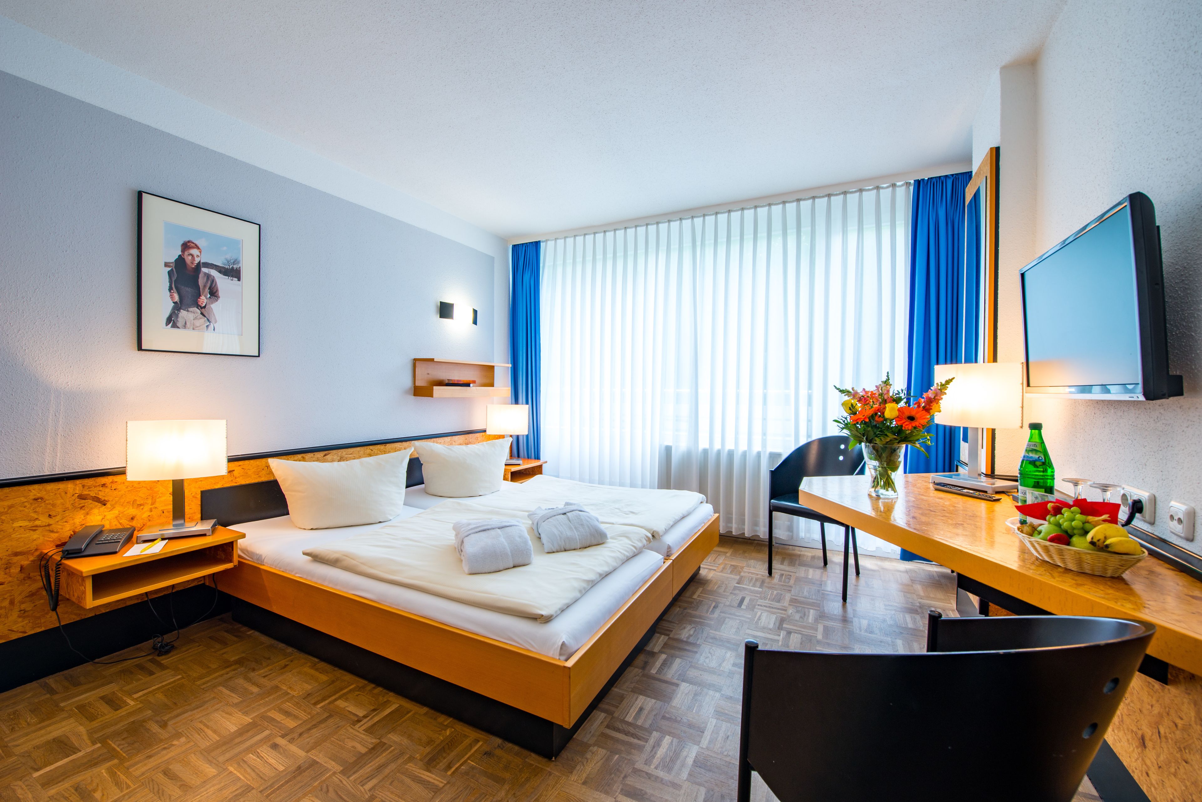 A hotel room with a bed, bedside table, lamp, chair, desk, and a television.