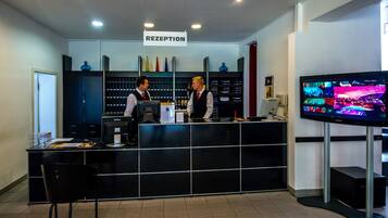 Un área de recepción con mostrador, dos recepcionistas, un cartel sobre el mostrador que dice