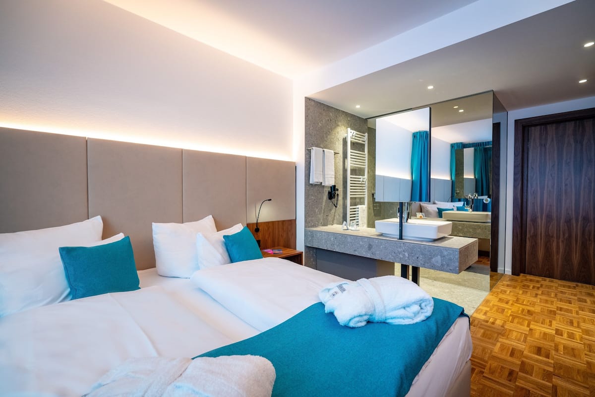Una habitación de hotel moderna con una cama grande, un baño con espejo y suelo de madera.