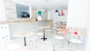 Een moderne keuken met een betegelde spatwand, een ingebouwde oven en een koffieapparaat. Er staan meerdere barkrukken en tafels met bloemenlinnen.