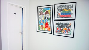 Een gang met drie ingelijste kunstwerken aan de muur en een witte deur met een nummerbord.