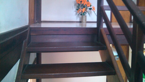 A wooden staircase with a vase of orange flowers on the landing. - Flat do Indio (Fernando de Noronha)