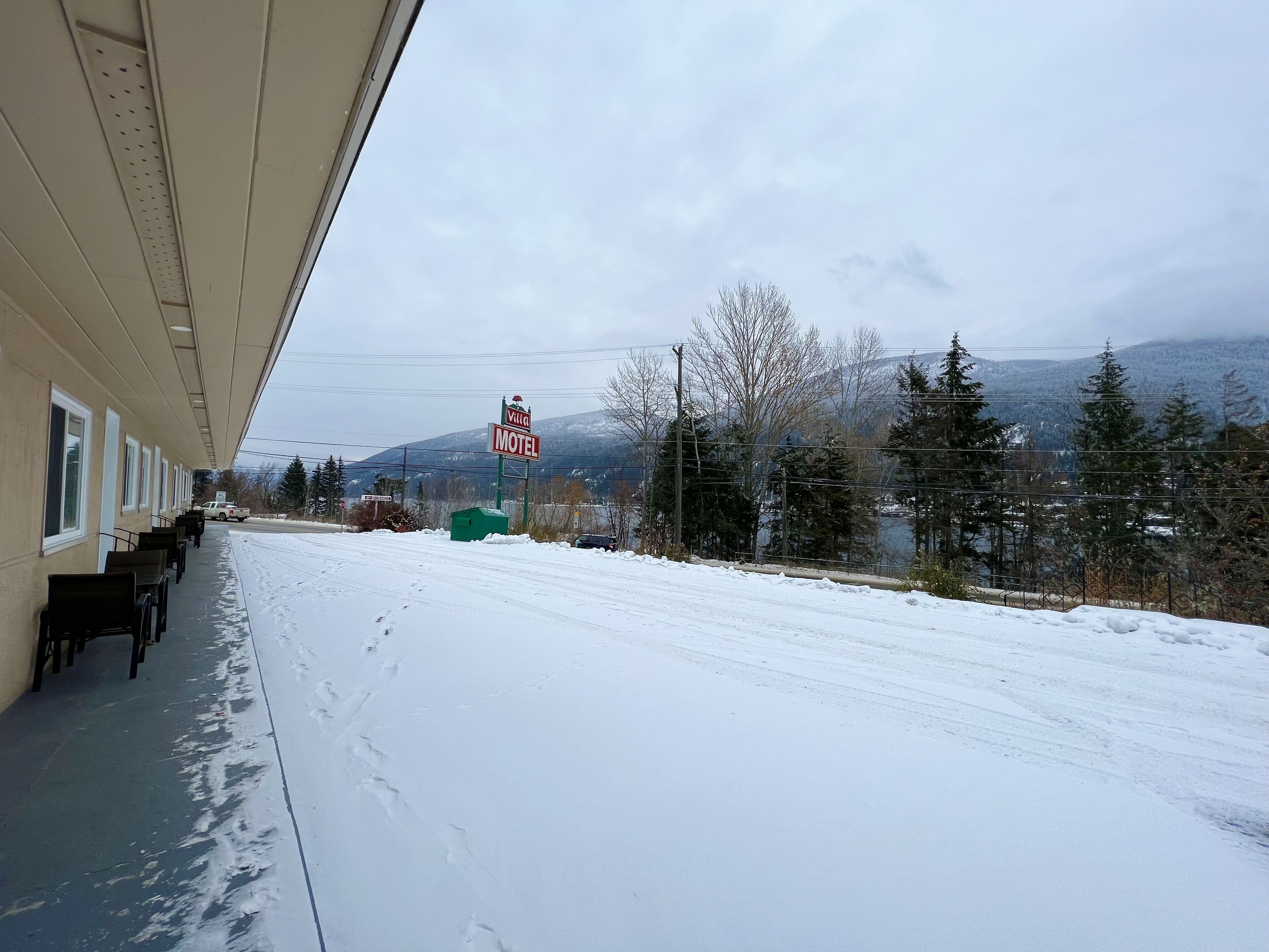 A motel with a covered outdoor seating area and a view of snow-covered mountains.