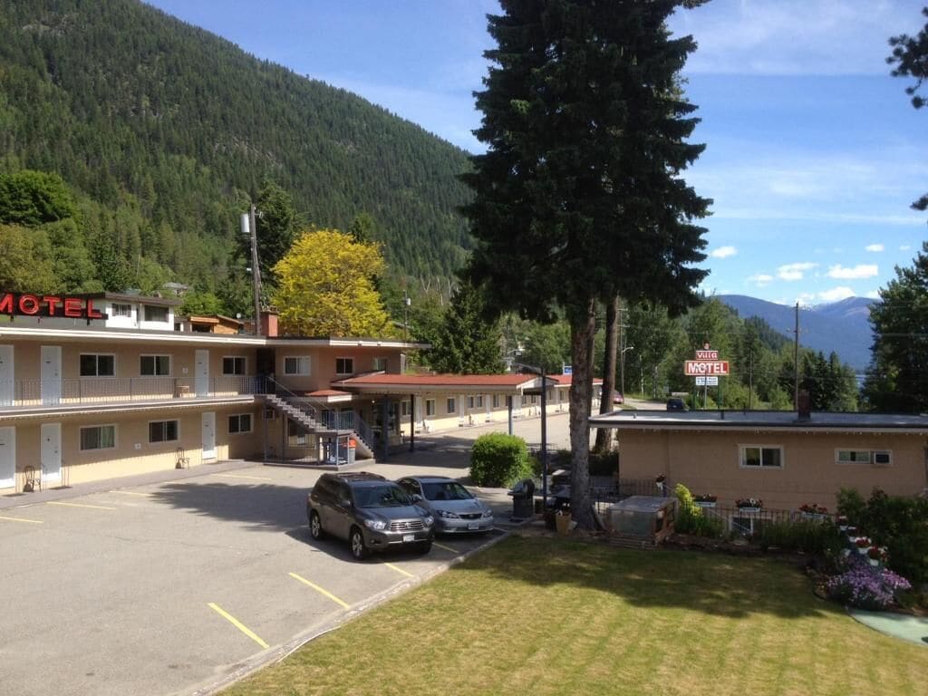 Un motel con estacionamiento, una escalera que lleva a la entrada y montañas al fondo.