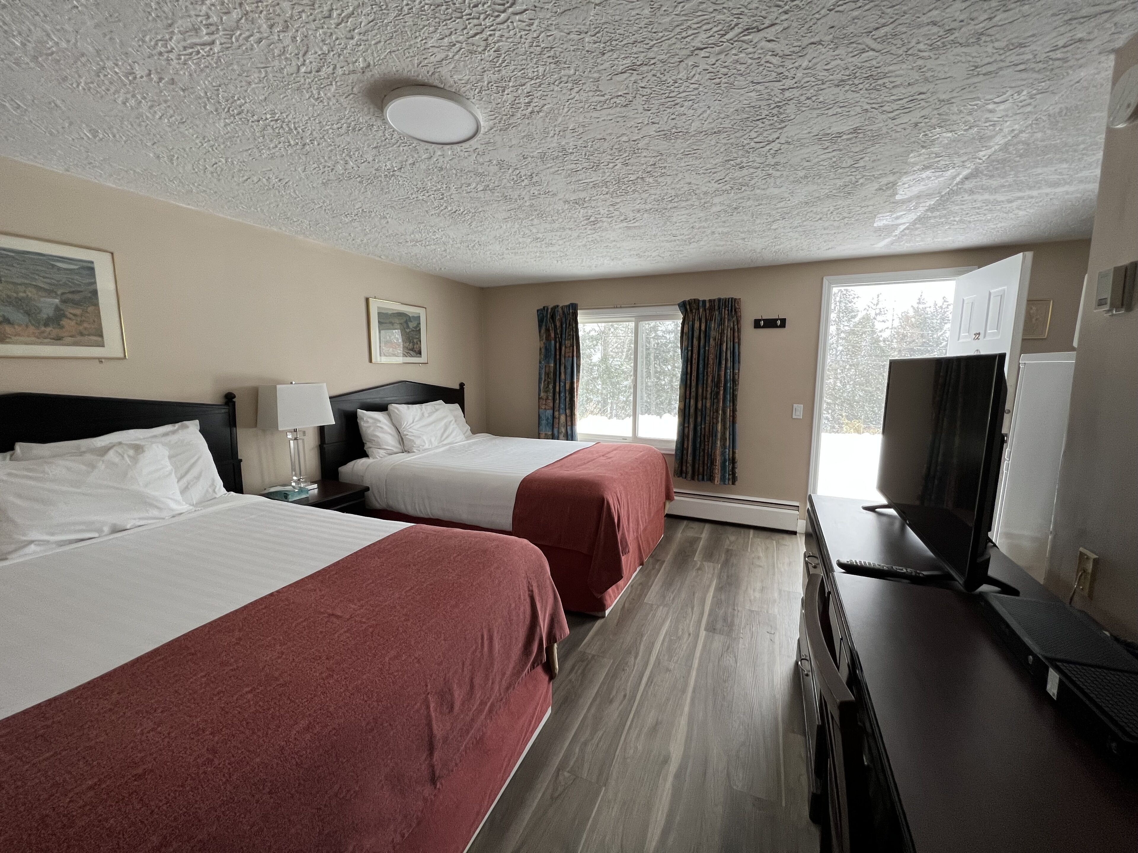 A hotel room with two beds, a desk with a computer, a TV, and a window with curtains.