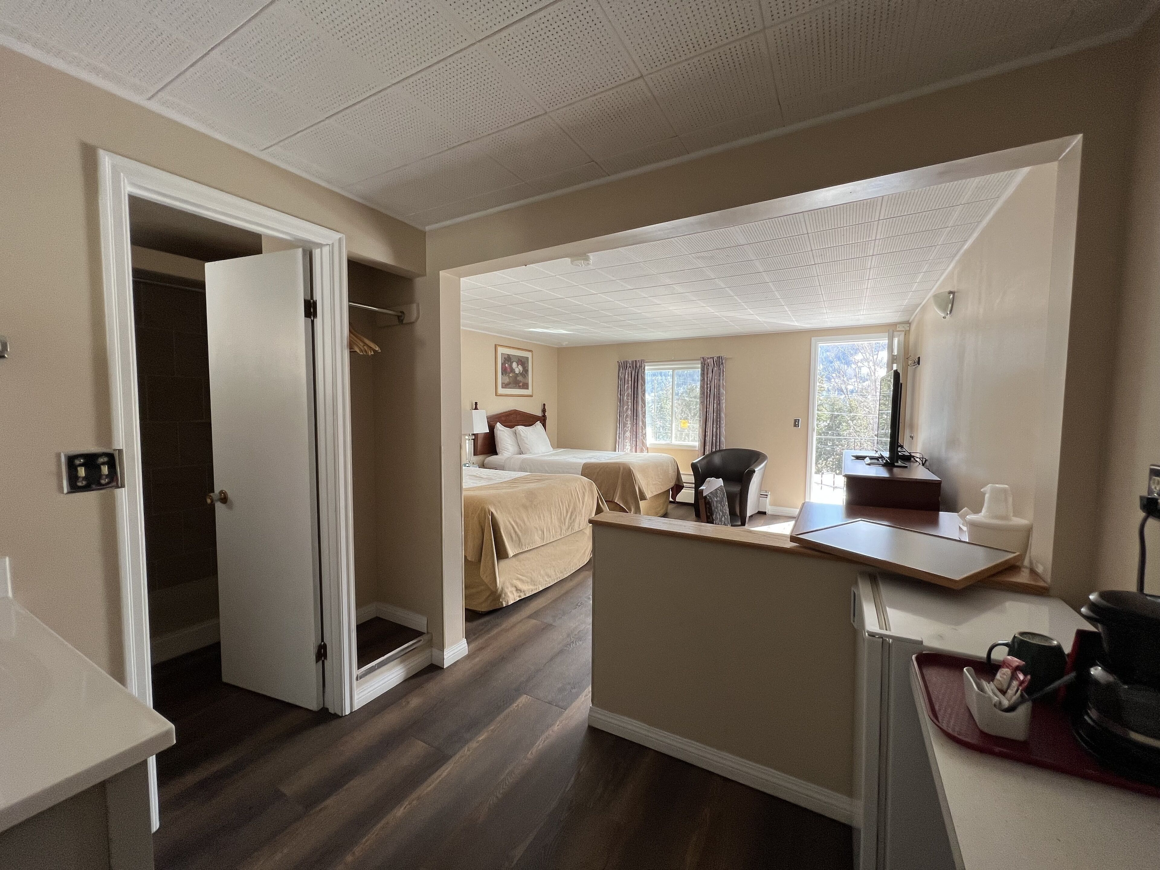 A hotel room with a bed, a desk, a chair, a window with curtains, a door, and a small balcony area.