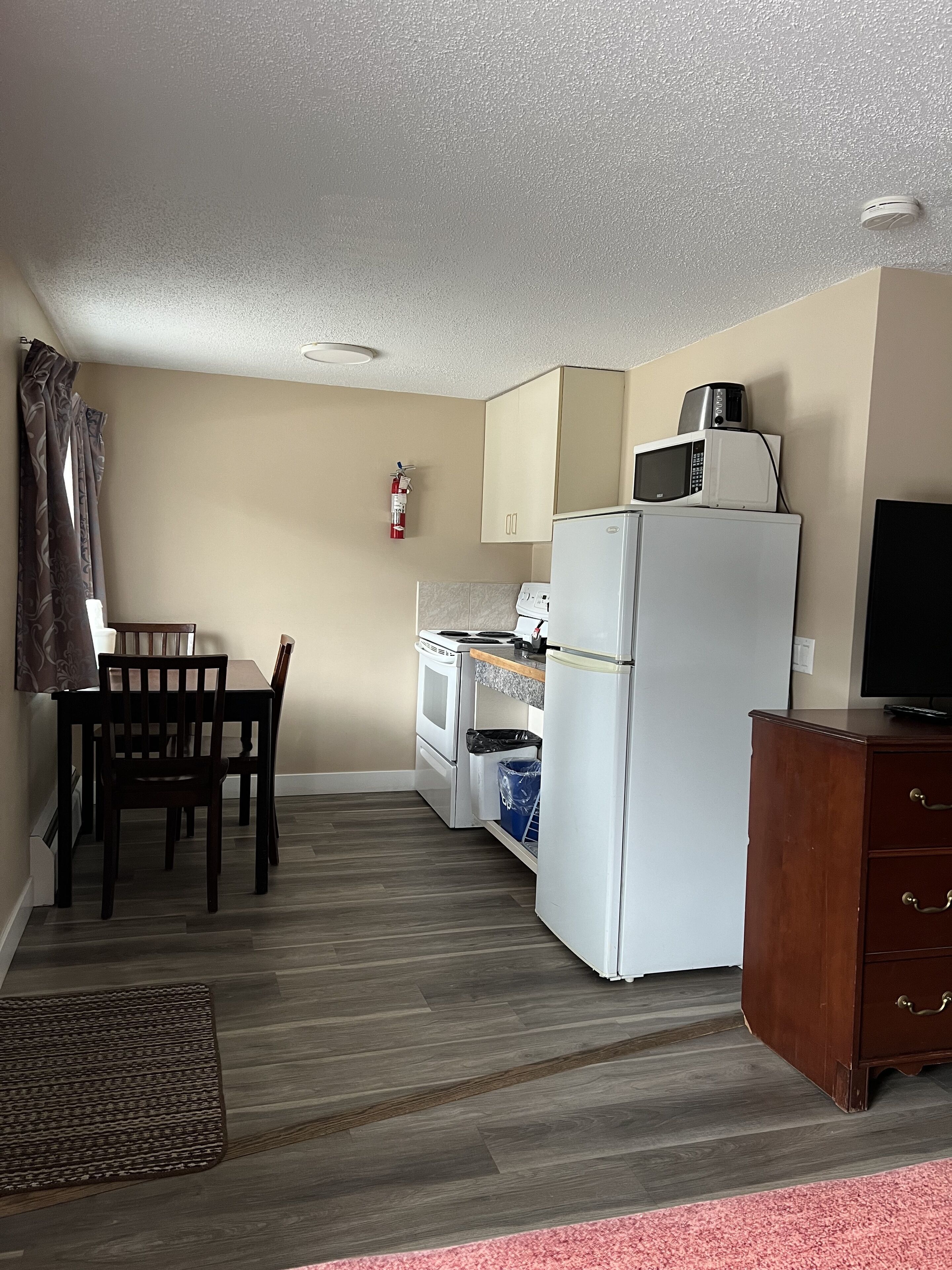 A compact kitchen with a dining area, a microwave, a refrigerator, and a fire extinguisher on the wall.