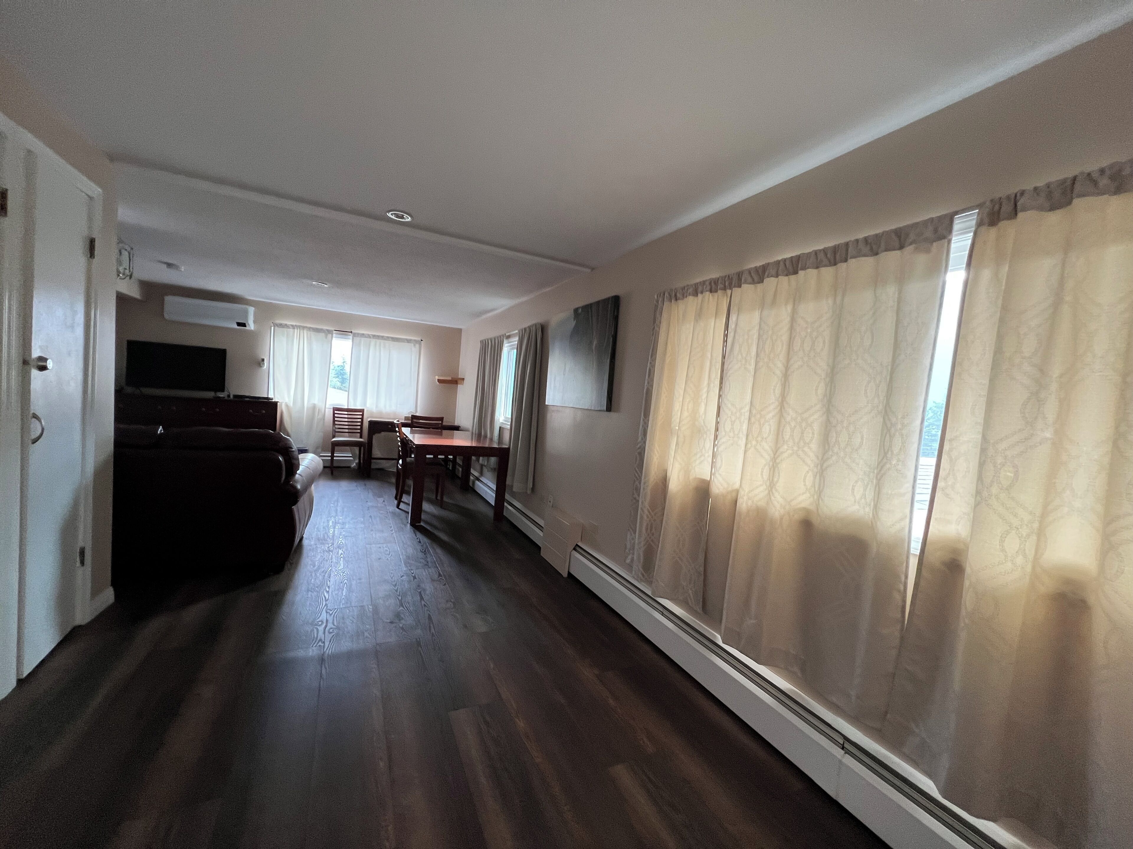 Amplia sala de estar con piso de madera oscura, una mesa de comedor con sillas, un sofá y una televisión.