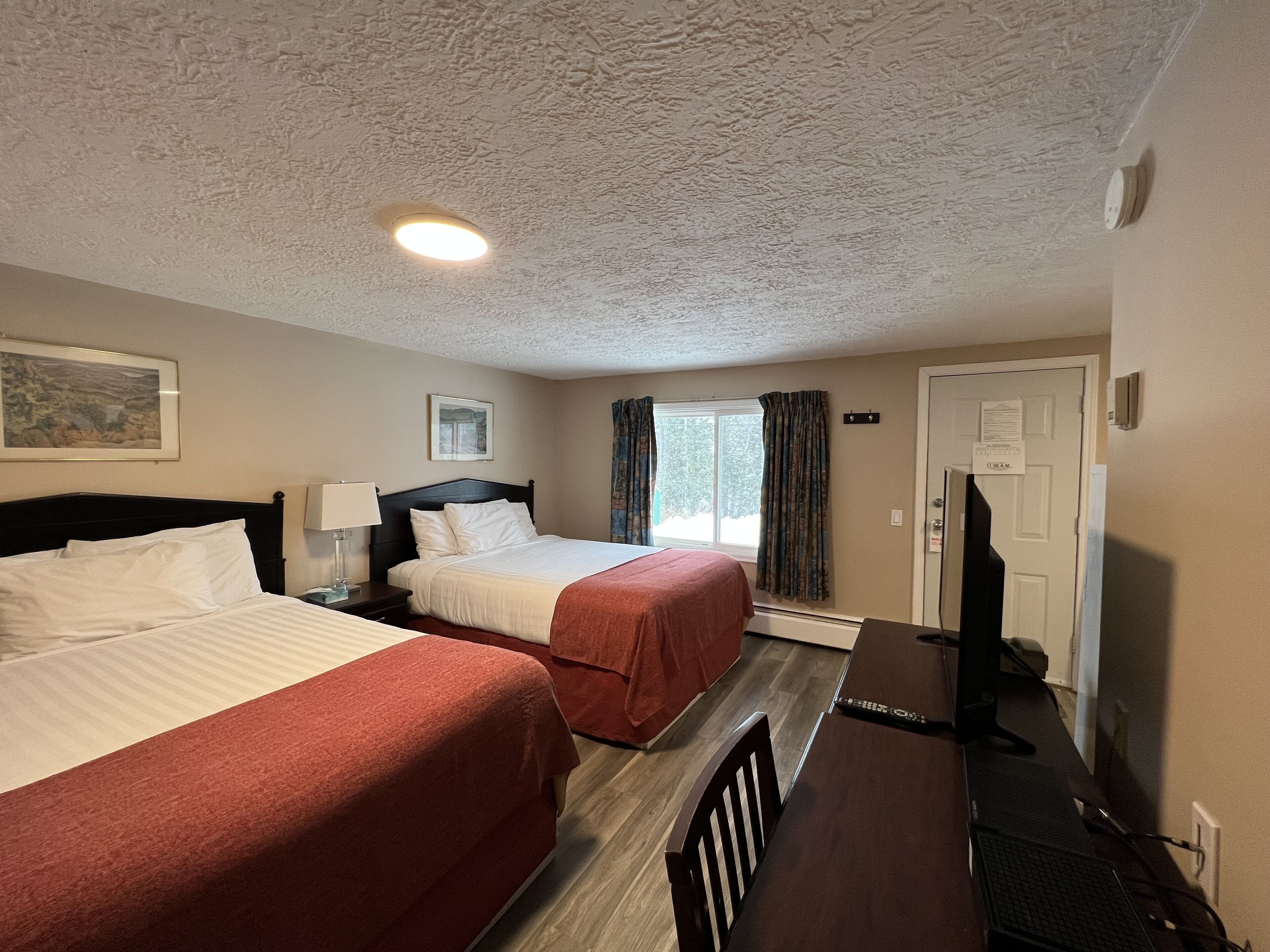 A hotel room with two beds, a desk, a chair, a TV, and a window with curtains.