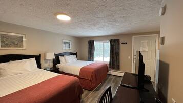 A hotel room with two beds, a desk, a chair, a TV, and a window with curtains.