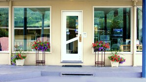 A building facade with a white door, large windows, and flower planters with red and purple flowers. - Villa Motel (Nelson)