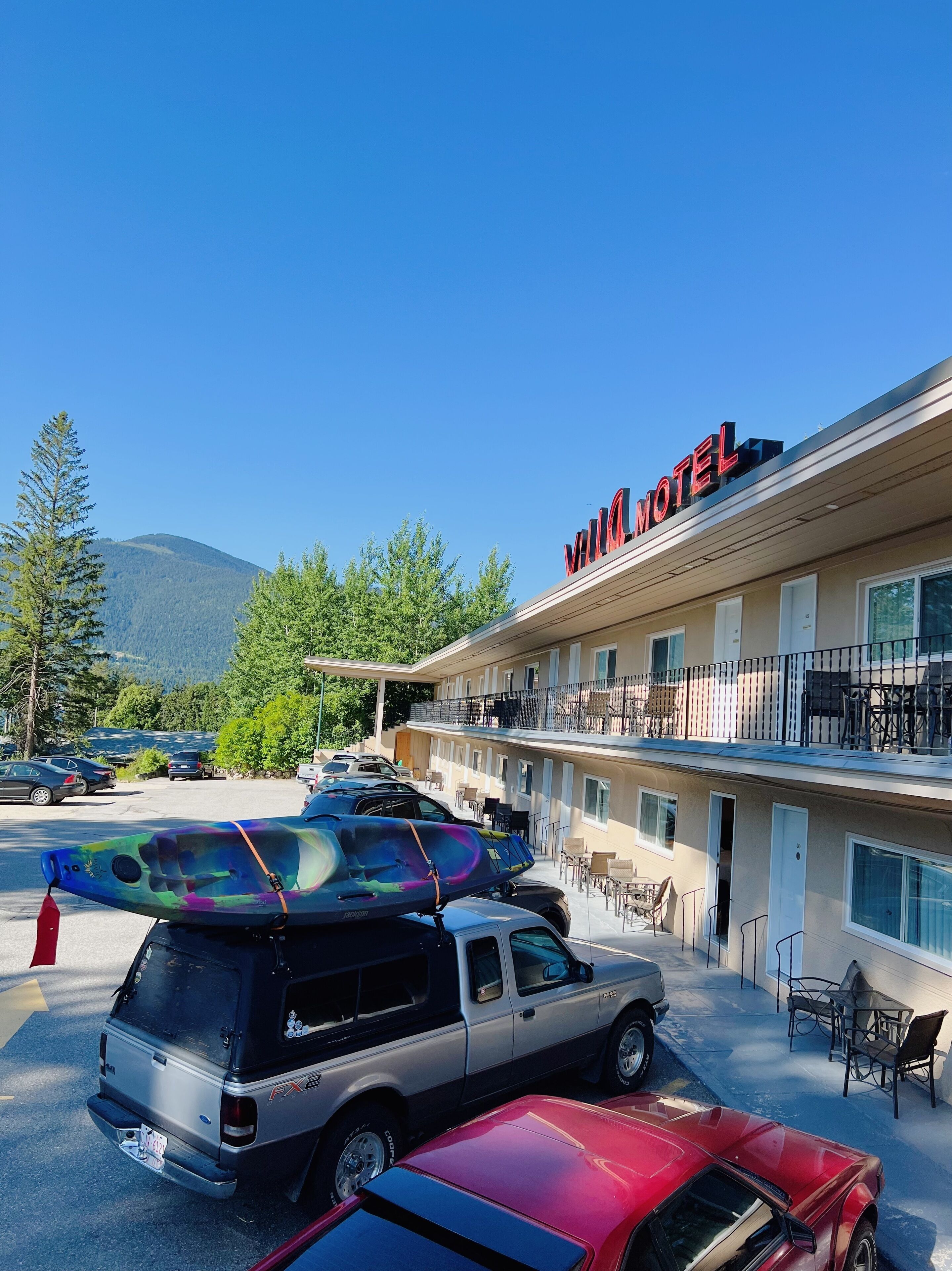 Un motel composé d’un bâtiment à deux étages, d’un espace extérieur aménagé avec des sièges et d’un parking où sont stationnés plusieurs véhicules.